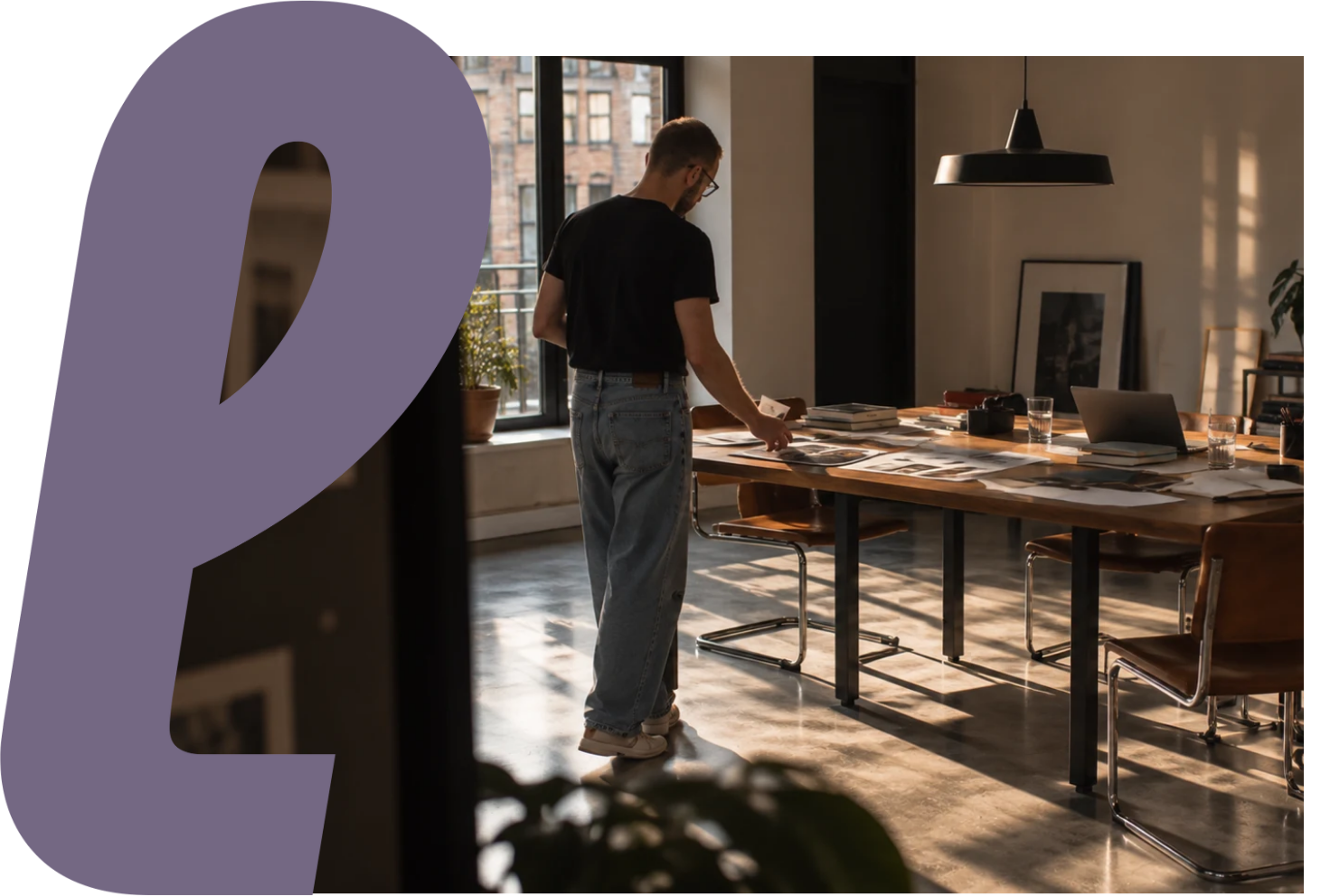 Bruno revisando materiais sobre uma mesa longa, com o monograma roxo da Palpitaria.